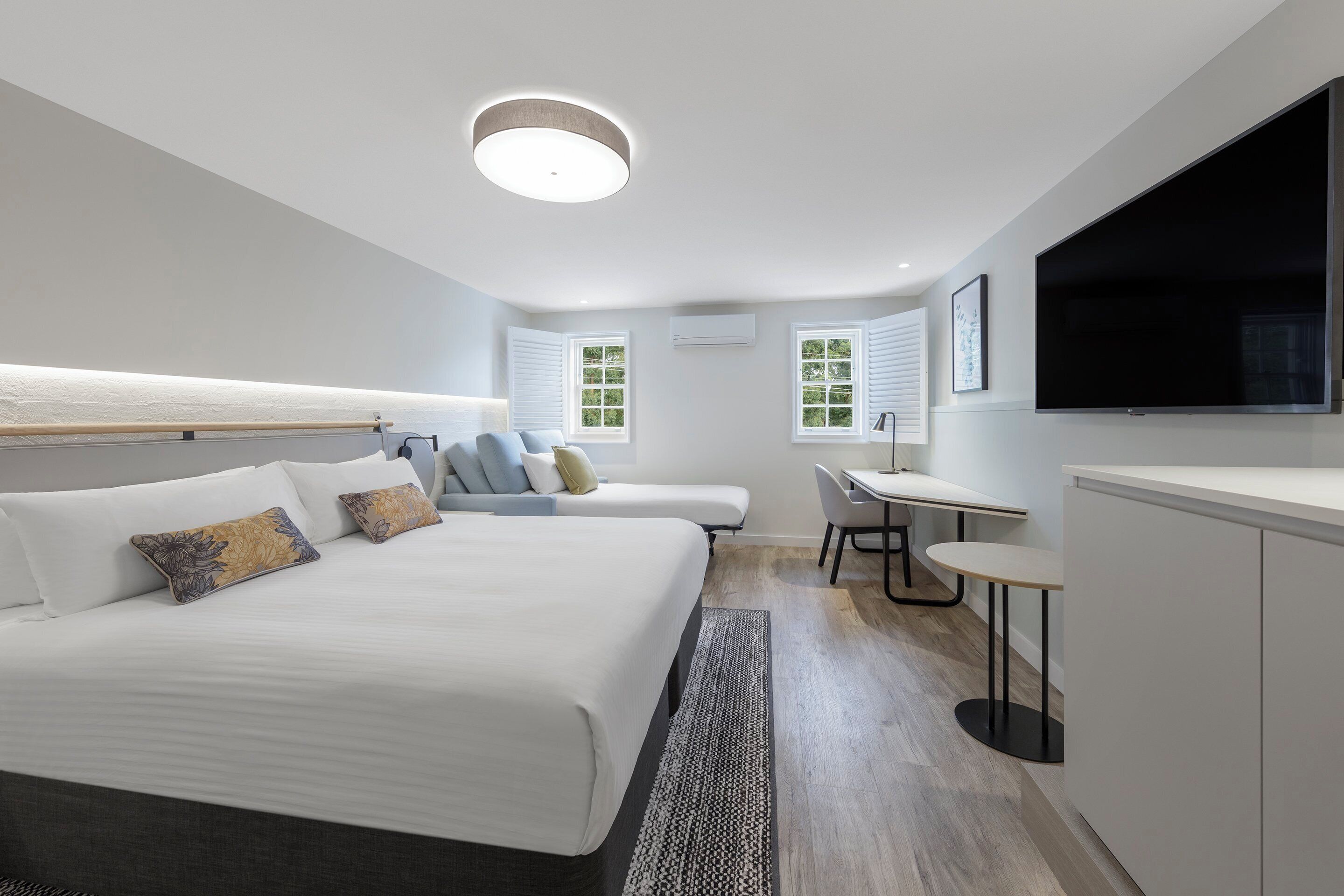 A modern hotel room with a large bed, a desk, a chair, and a television.