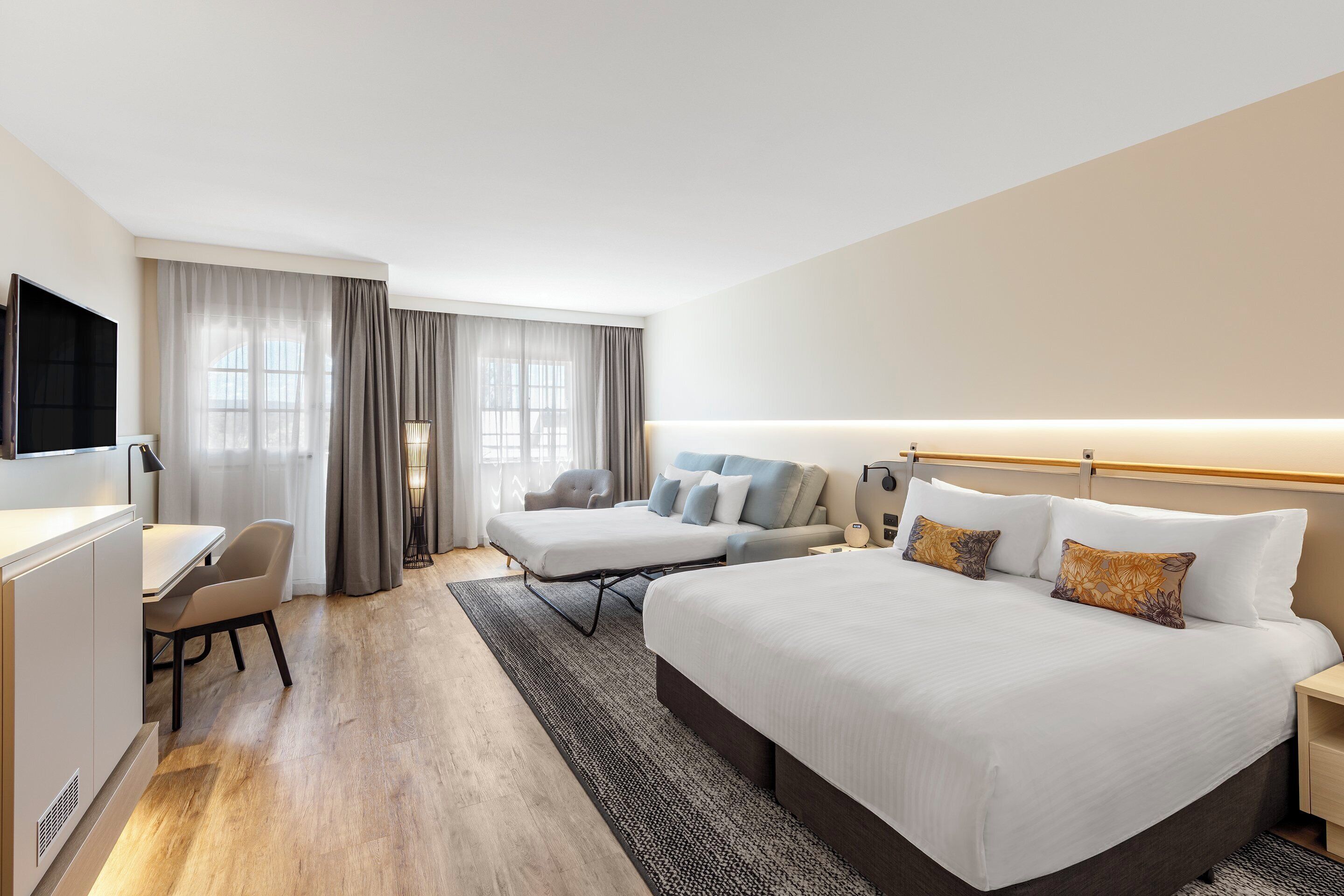 A hotel room with a bed, bedside tables, a desk, and a chair.