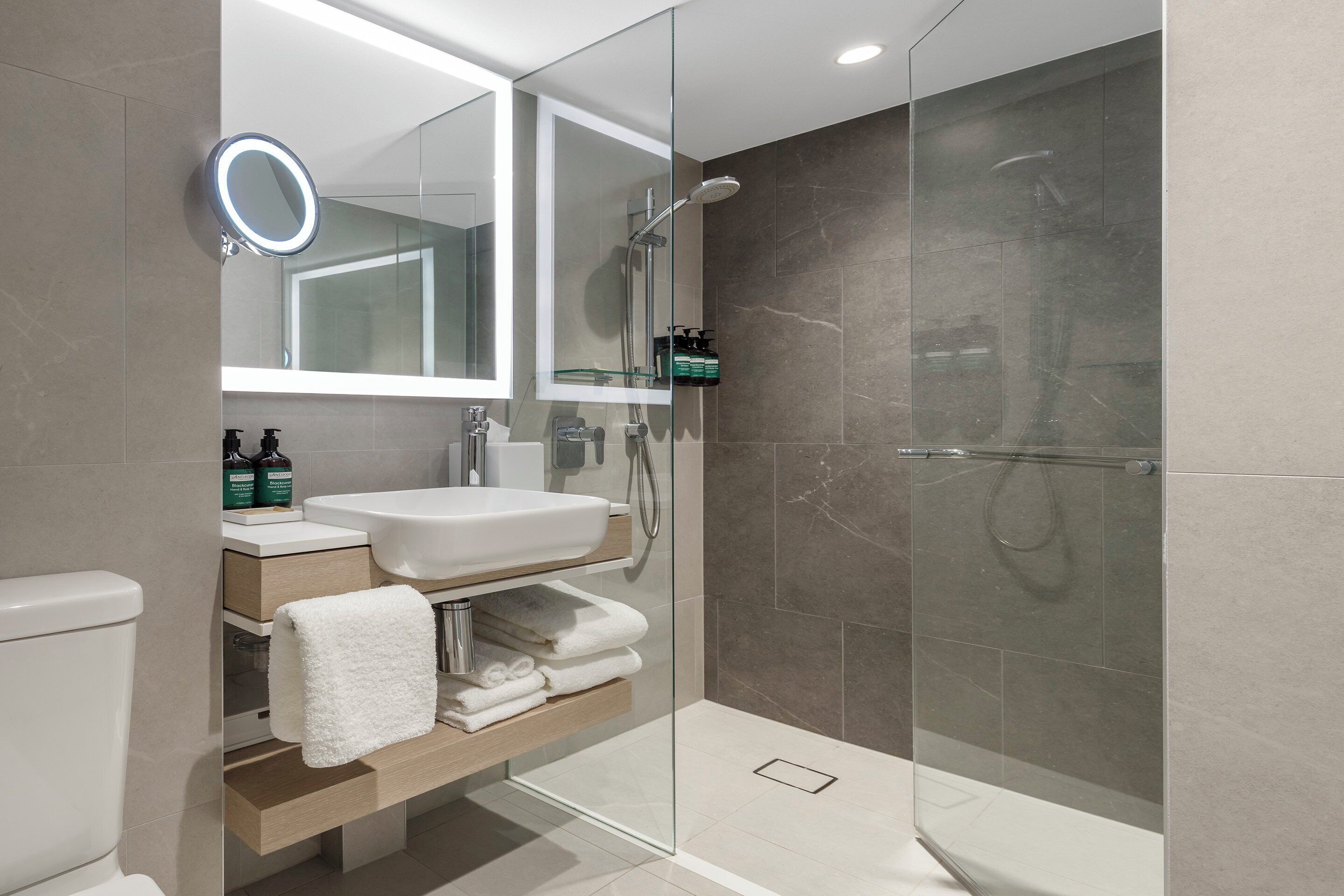 Un baño moderno con ducha de vidrio, un lavabo blanco y un espejo con luz.