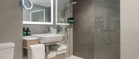 Un baño moderno con ducha de vidrio, un lavabo blanco y un espejo con luz.