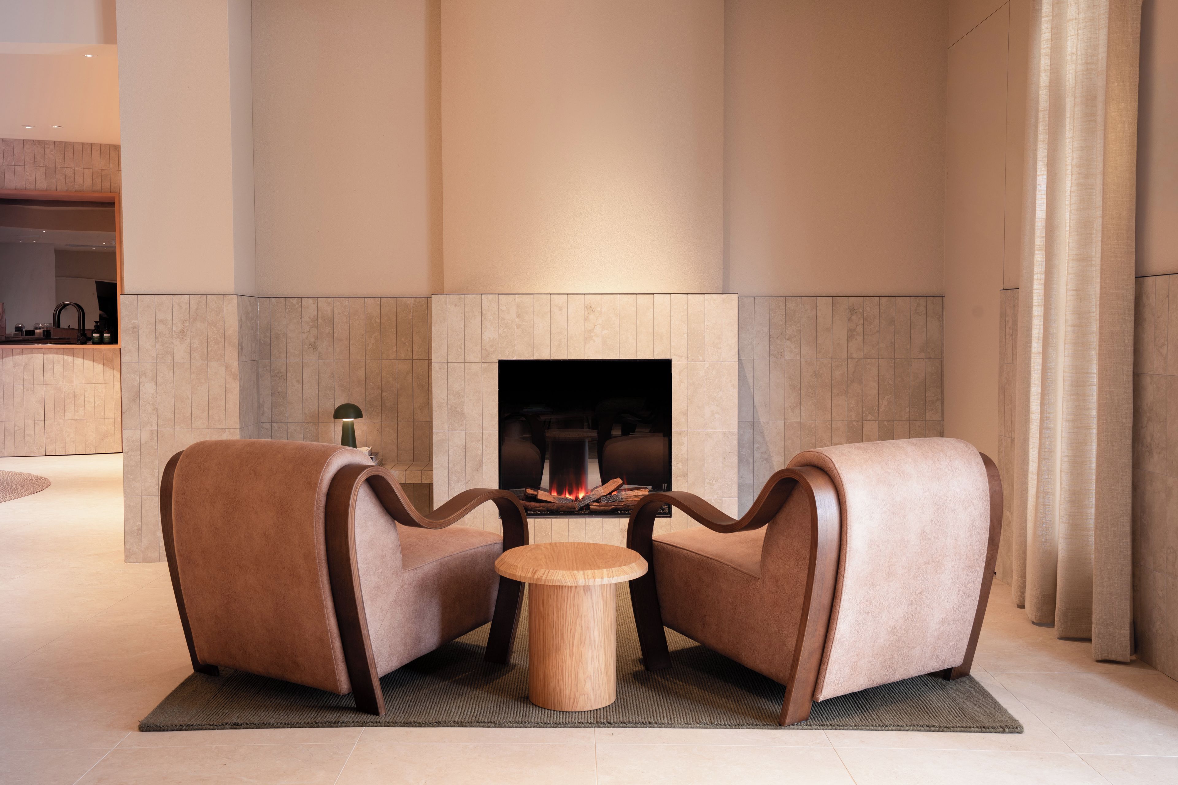 Een moderne zithoek met een open haard, twee leren fauteuils en een klein houten tafeltje.
