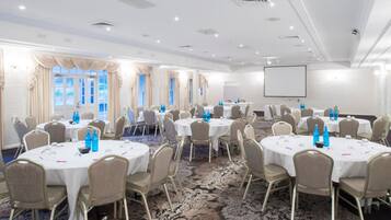 Un salón de conferencias con mesas redondas, sillas color beige y una pantalla grande.