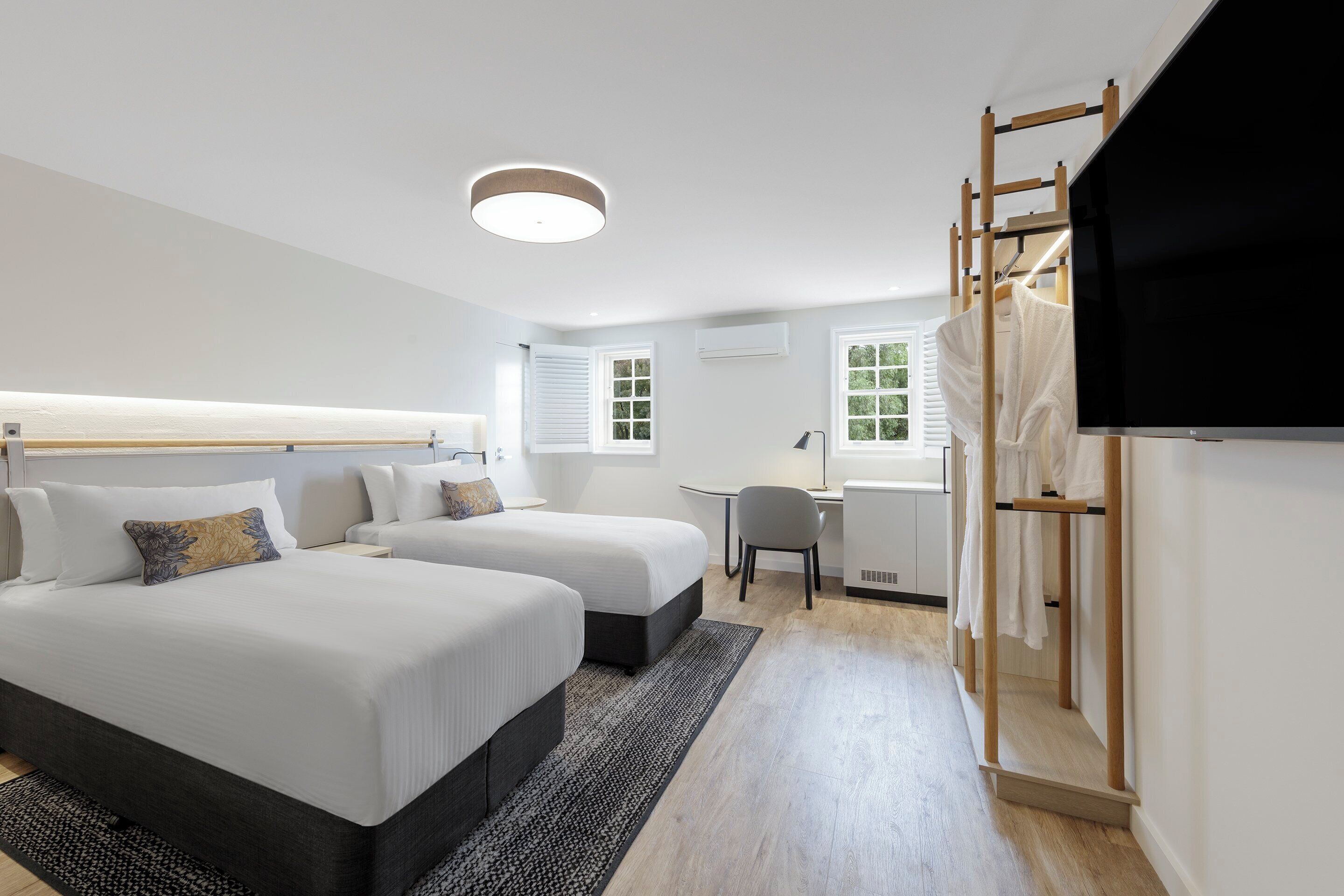 A hotel room with two beds, a desk, a chair, a TV, and a wardrobe.