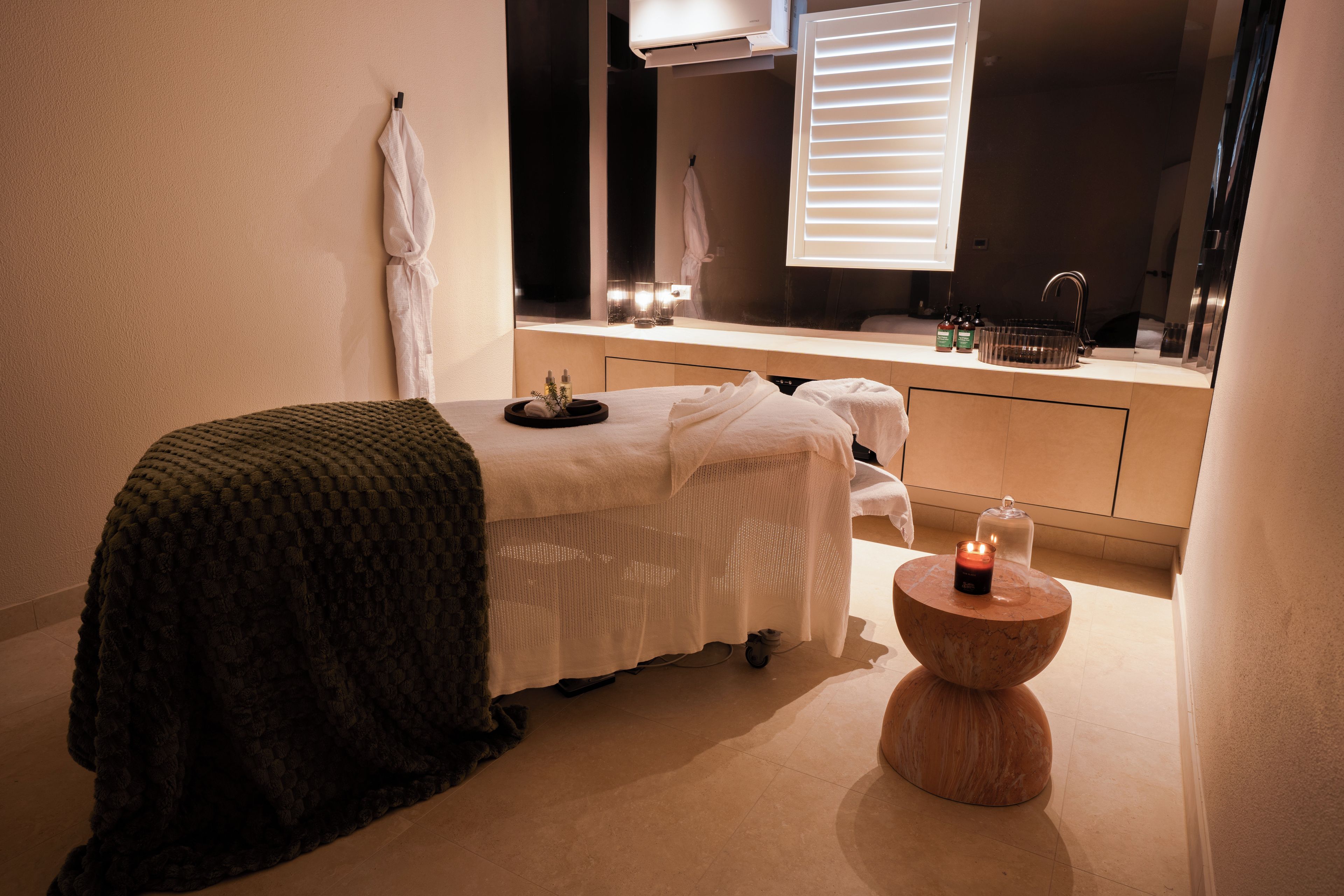 Un cuarto de spa con una camilla de masaje, una toalla, una vela y una pequeña mesa de madera.