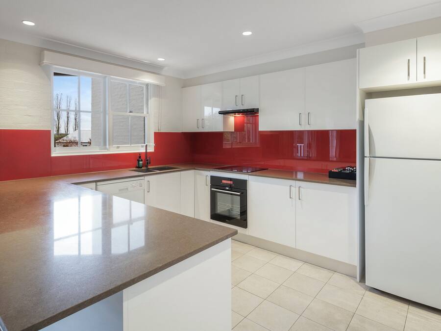 Une cuisine moderne avec des meubles blancs, un pare-feu rouge et un grand îlot central doté d’un comptoir en granit.