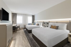 A hotel room with two beds, a desk, and a TV.