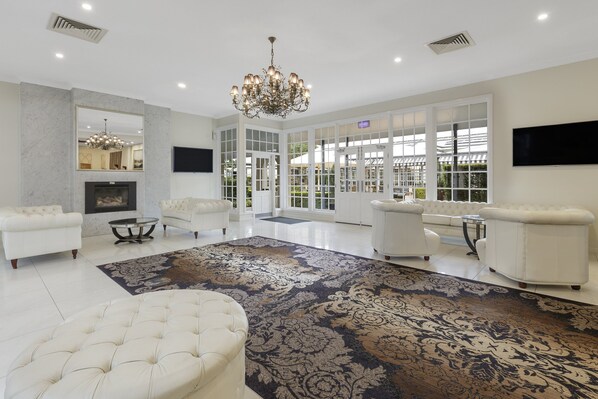 A spacious living room with a large chandelier, white sofas, a patterned rug, and a television mounted on the wall.