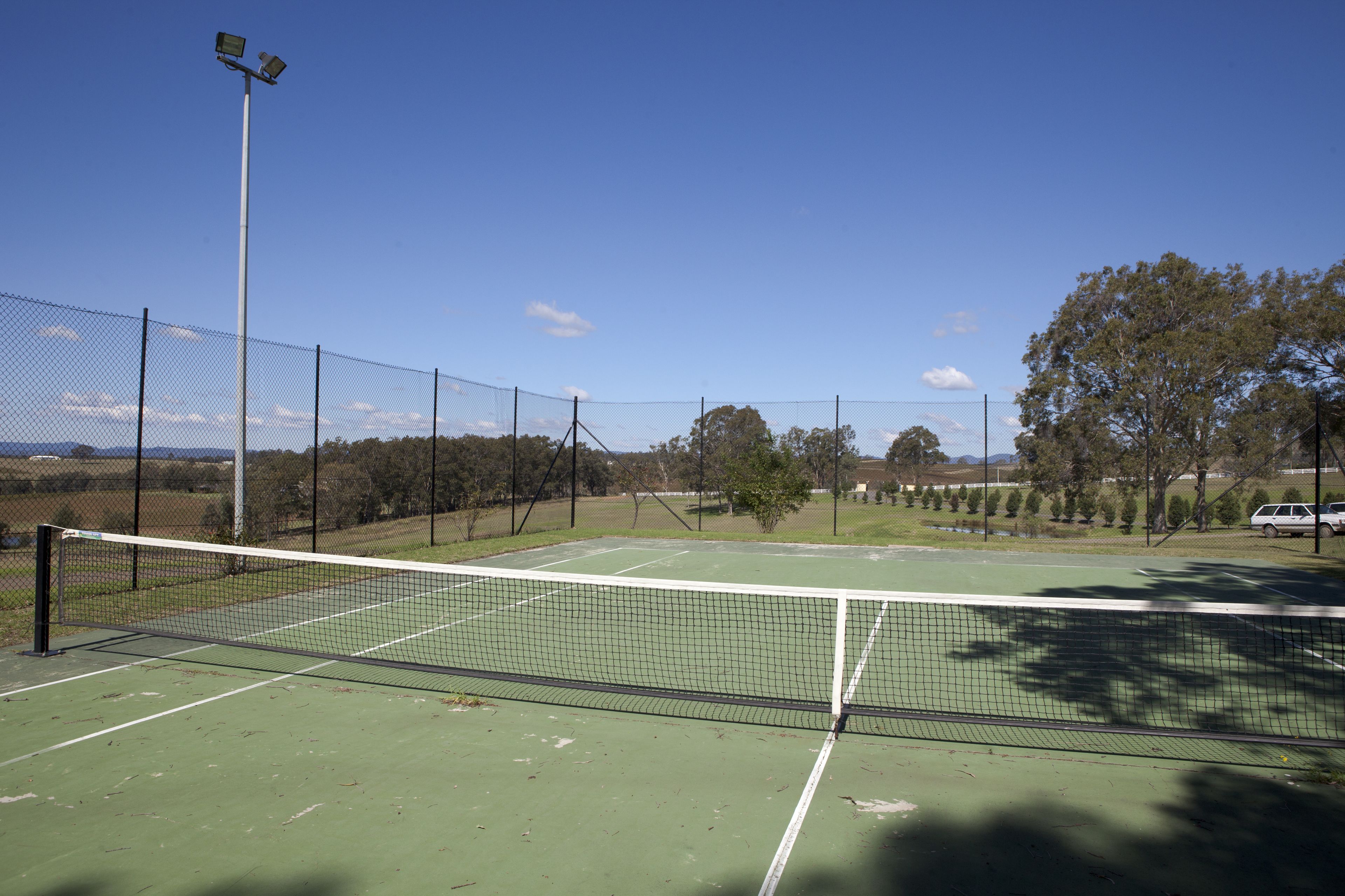A tennis court with a net, surrounded by a fence, and trees in the background.
