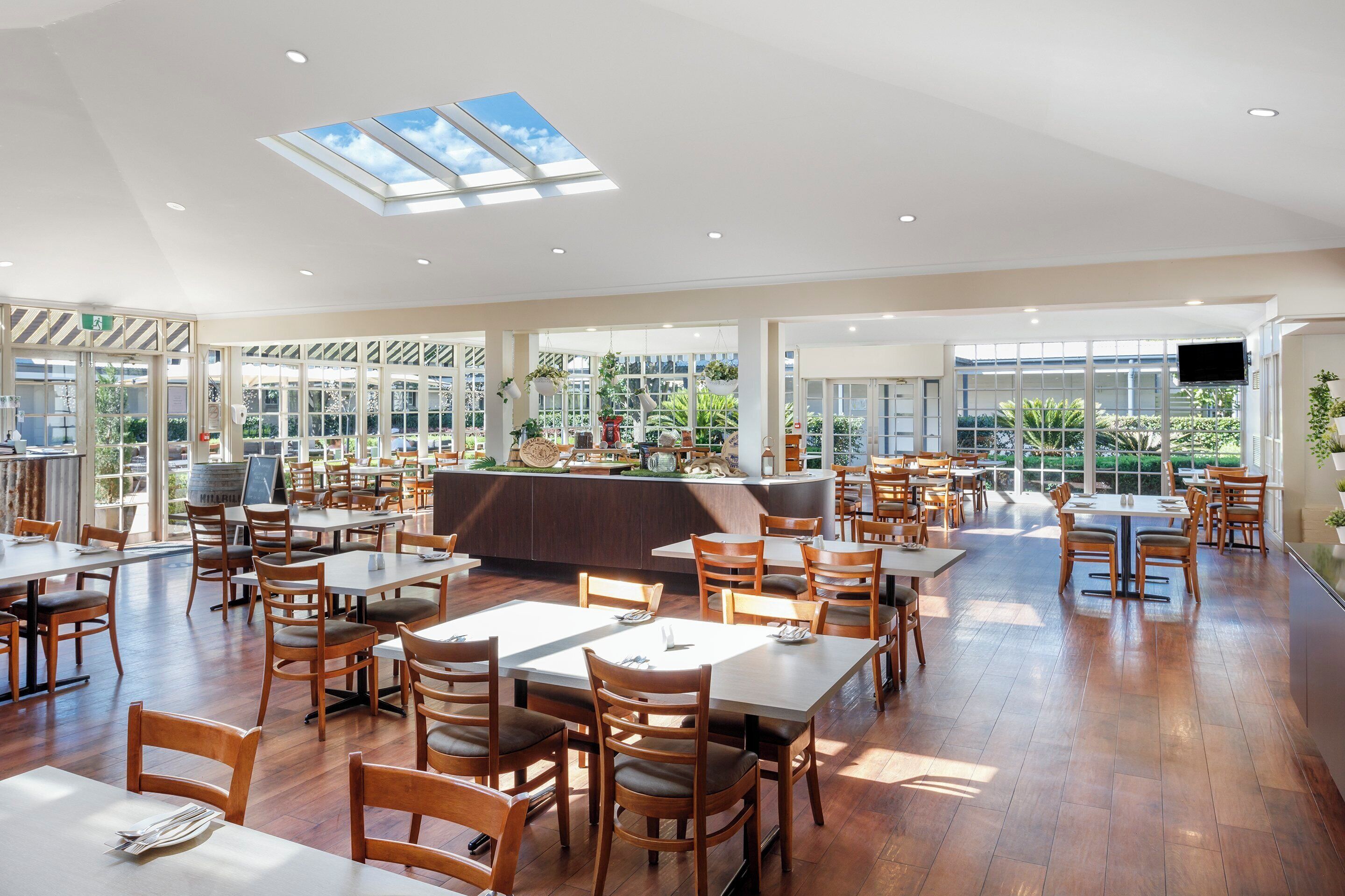 Un restaurant spacieux avec de hauts plafonds, de grandes fenêtres, ainsi que des tables et des chaises en bois.