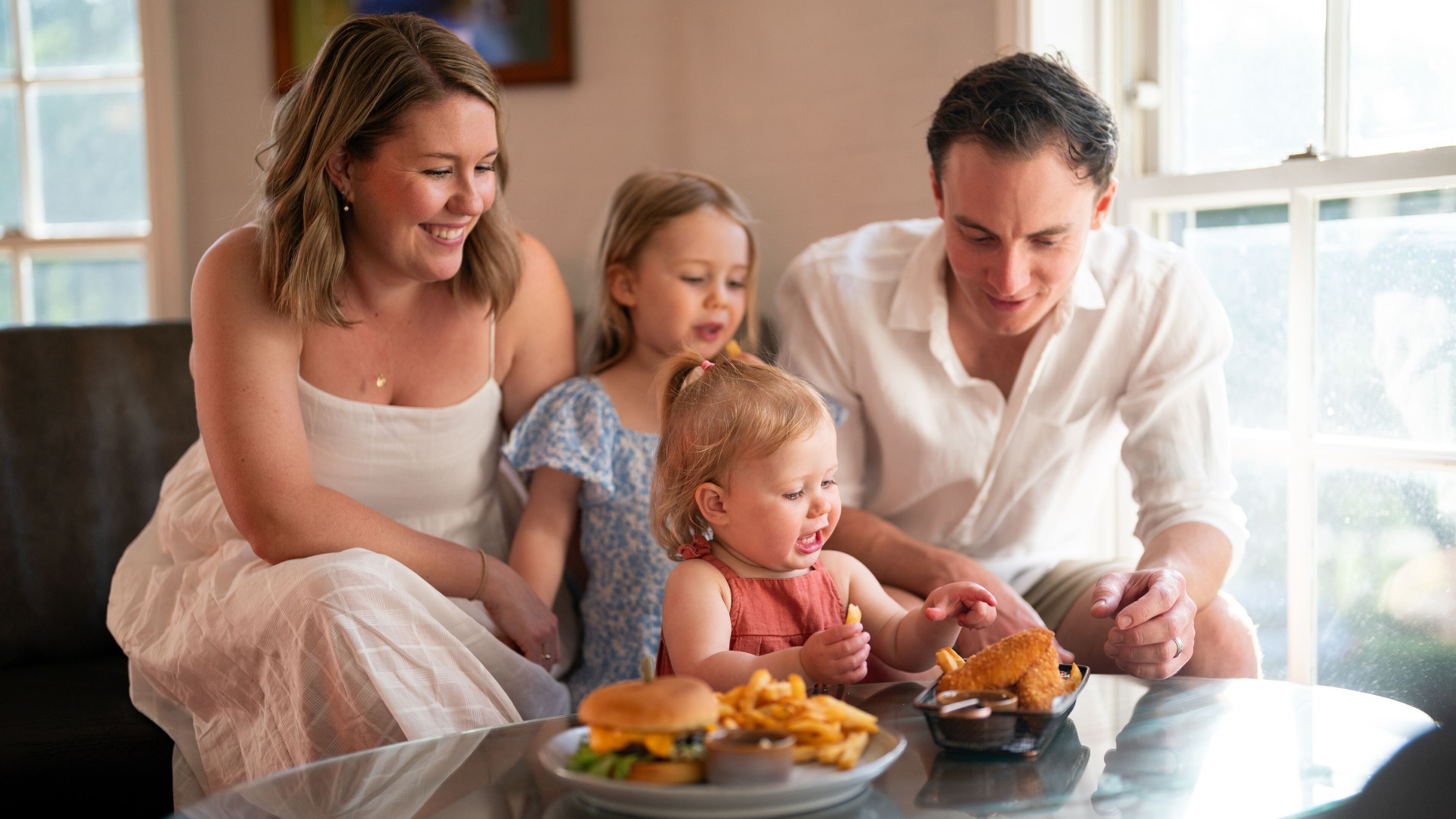 En familie spiser ved et bord med burger og pommes frites.
