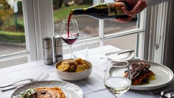 A dining table with a bottle of wine being poured into a glass, a bowl of food, and plates with food remnants.