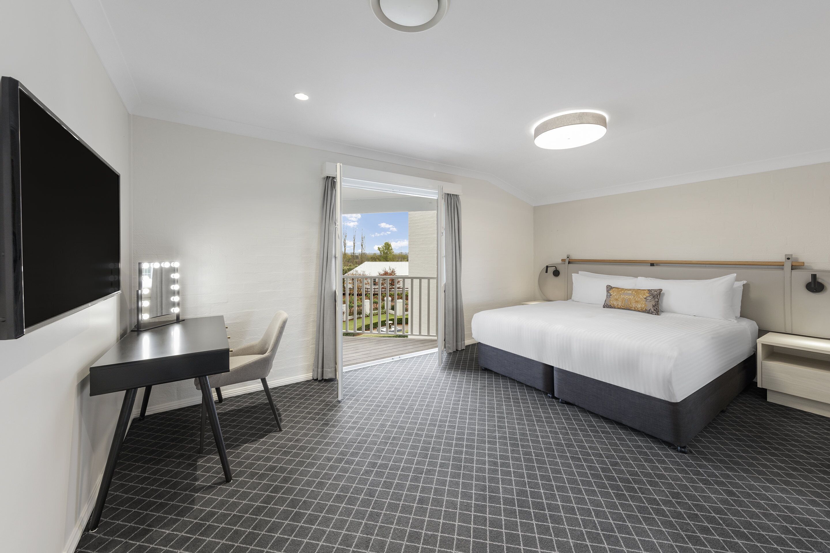 A modern hotel room with a large bed, a desk, and a balcony with a view.