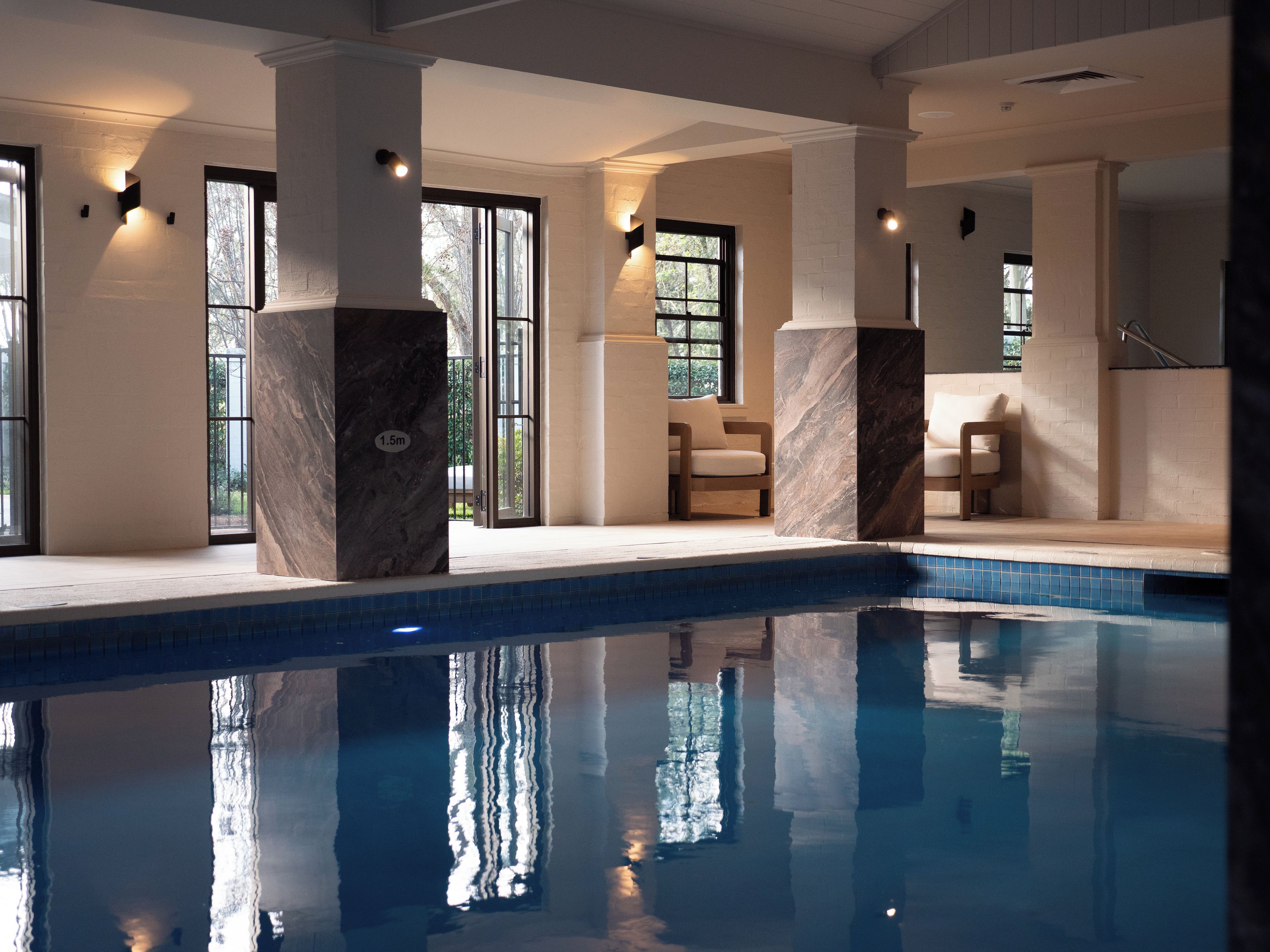 A swimming pool with clear water, surrounded by white walls and large pillars, with windows allowing natural light.