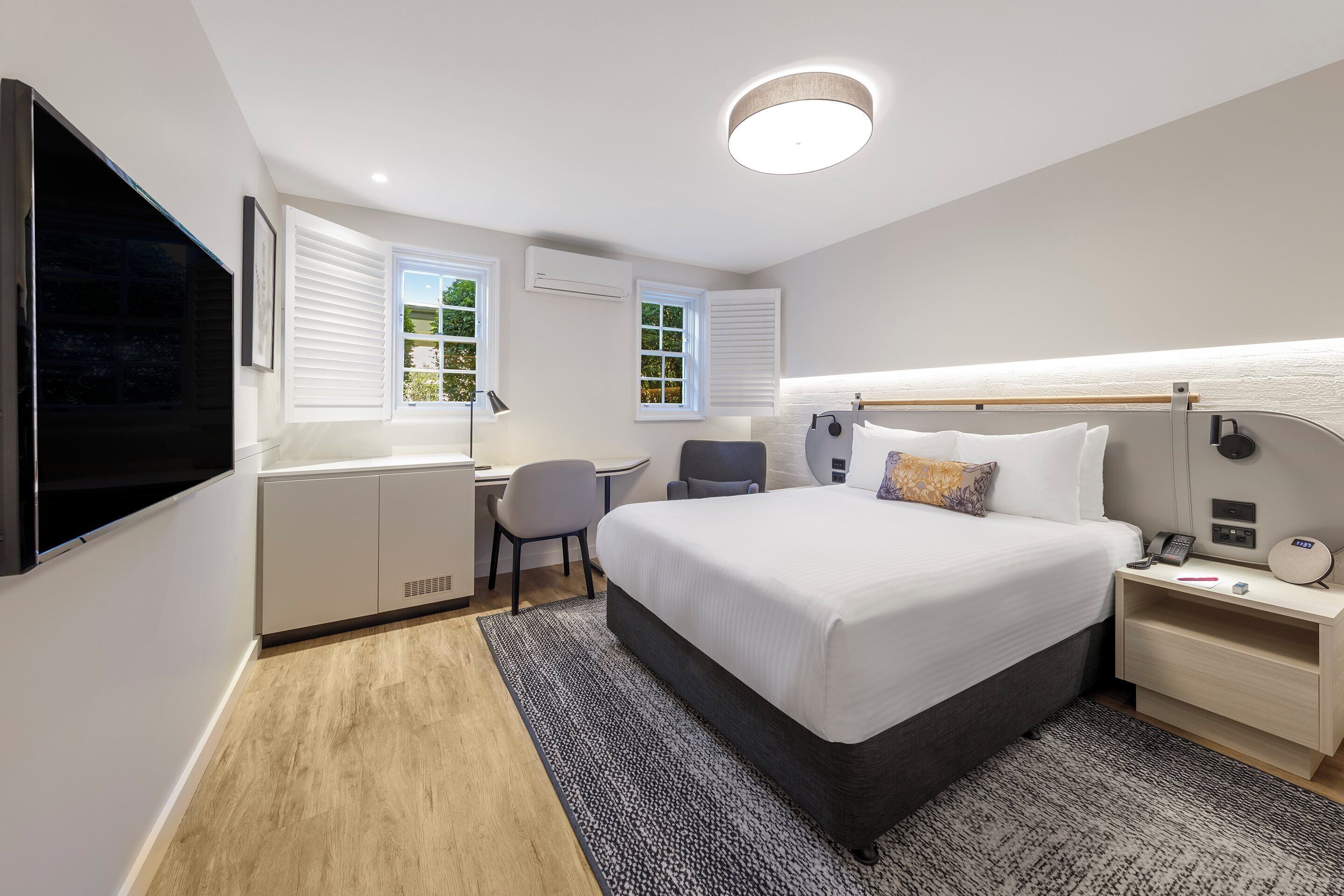 Habitació d'hotel moderna amb un llit, una taula de nit, escriptori, cadira i una televisió.