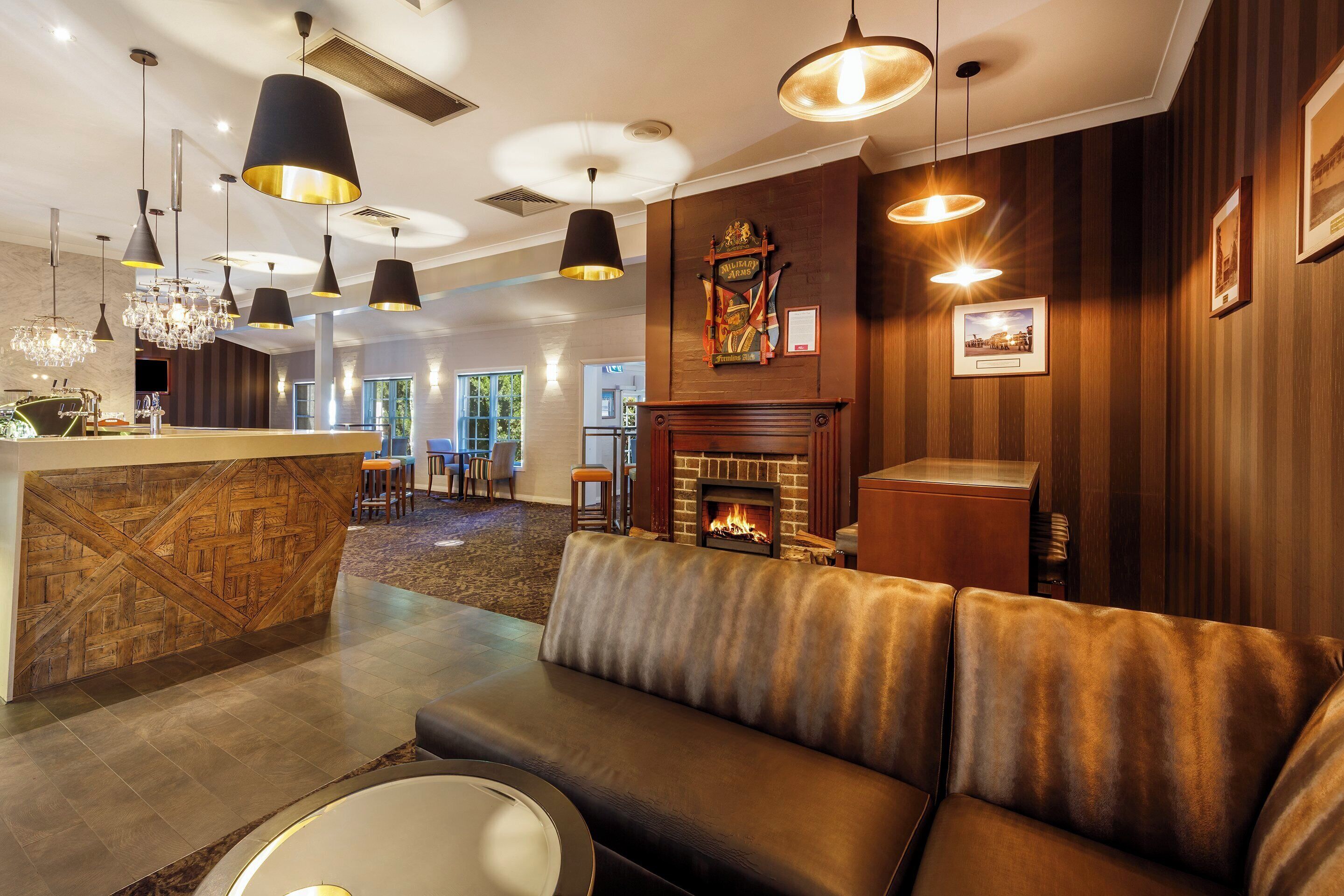 Un área de descanso moderna con chimenea, sofá de cuero y bar con un revestimiento de pared de madera.