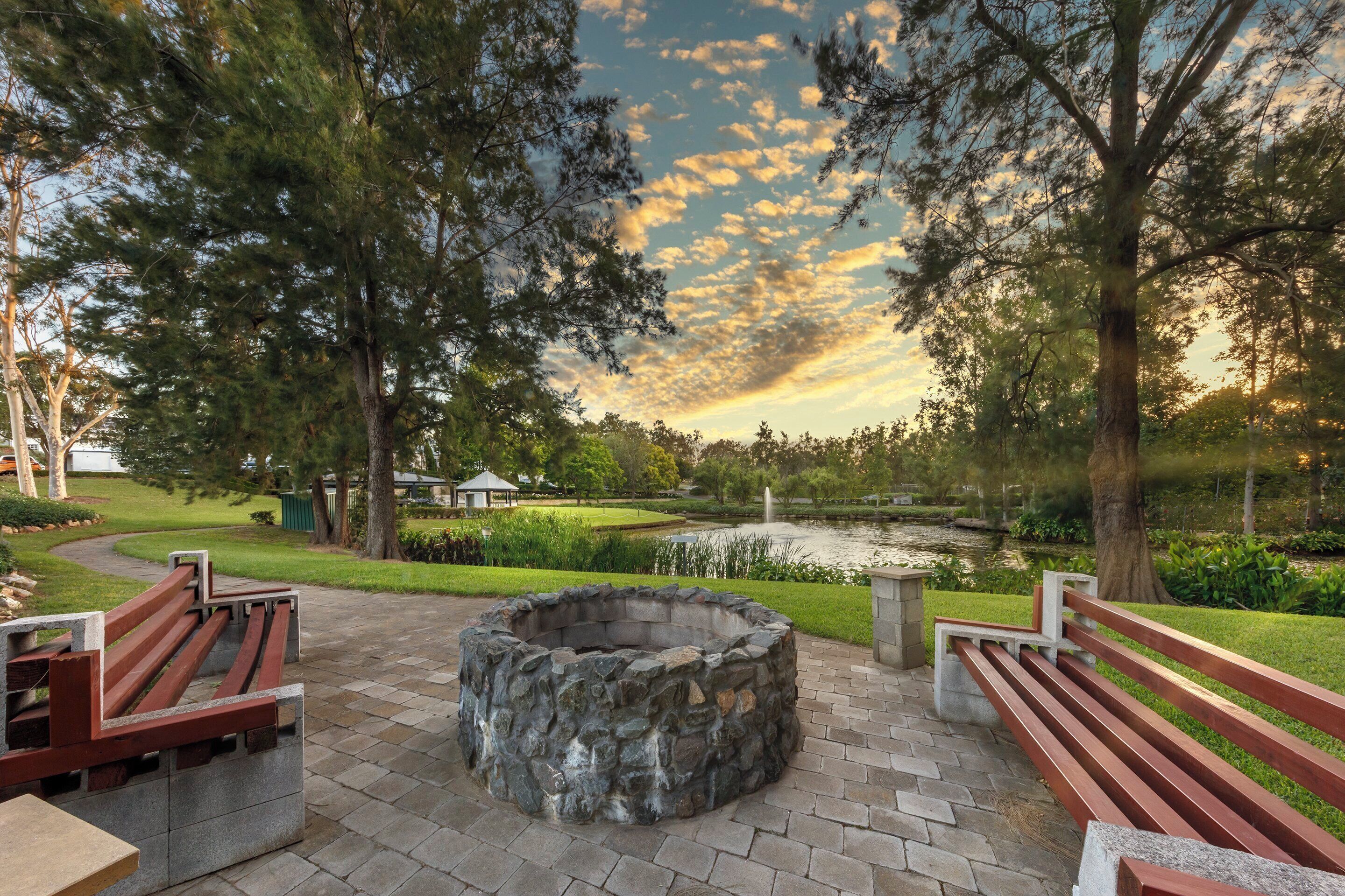 A park with a stone fire pit, benches, and a pond.