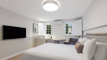 A modern hotel room with a large bed, a flat-screen TV, a desk, and two windows with blinds.