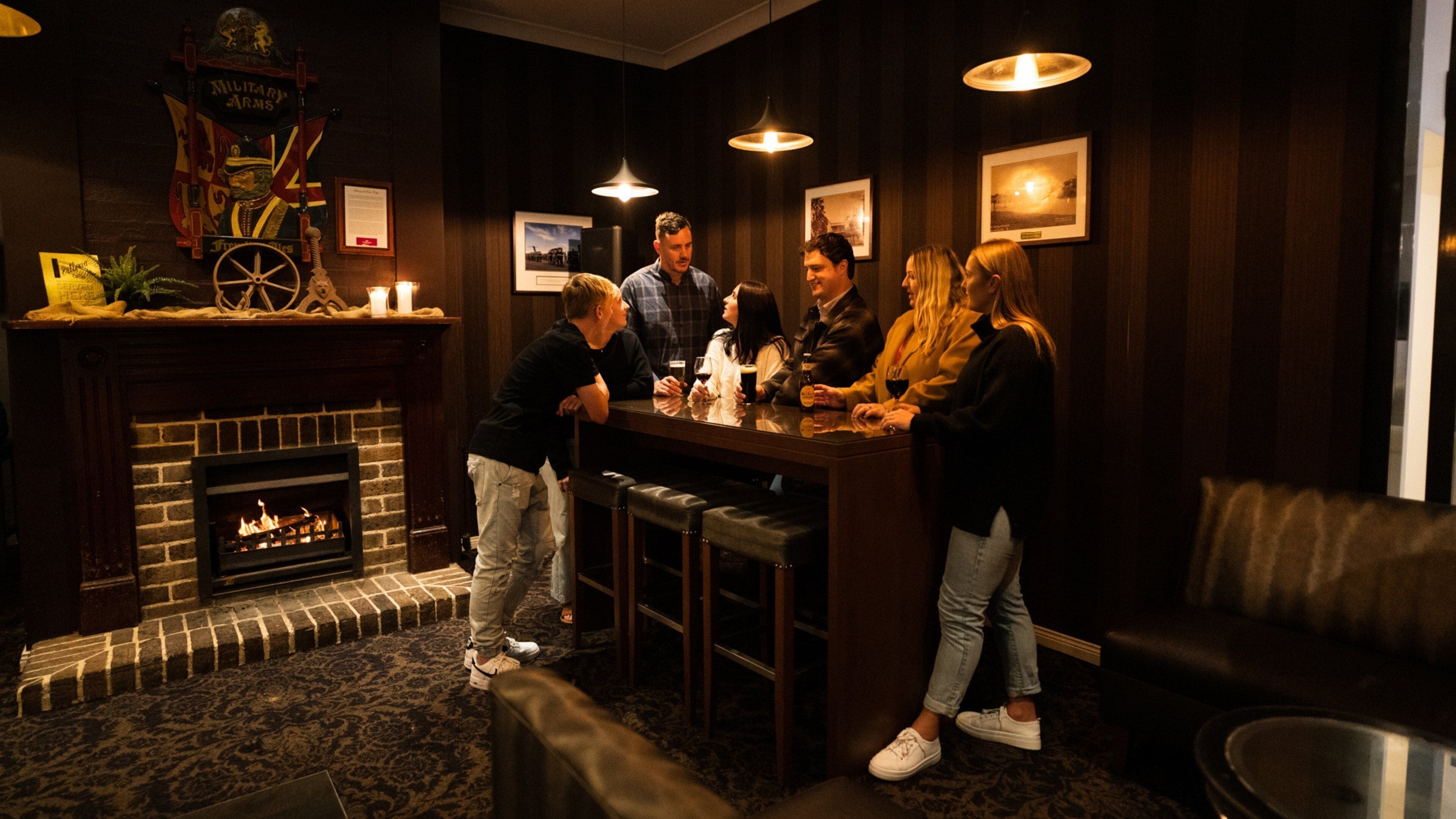Zona de bar con chimenea, paredes de madera y un grupo de personas conversando.