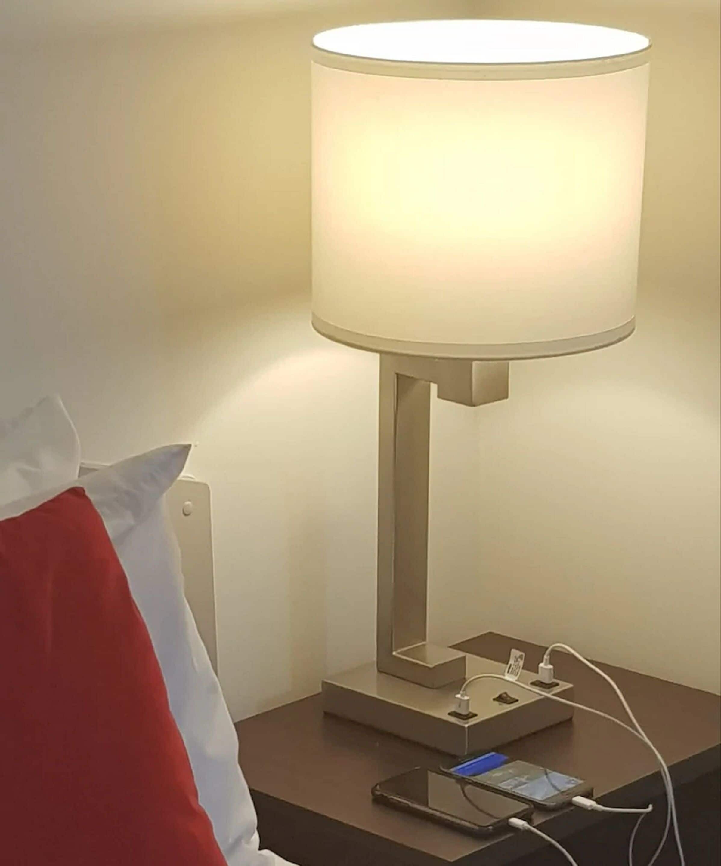 A bedside table with a lamp, a smartphone, and a charging cable.