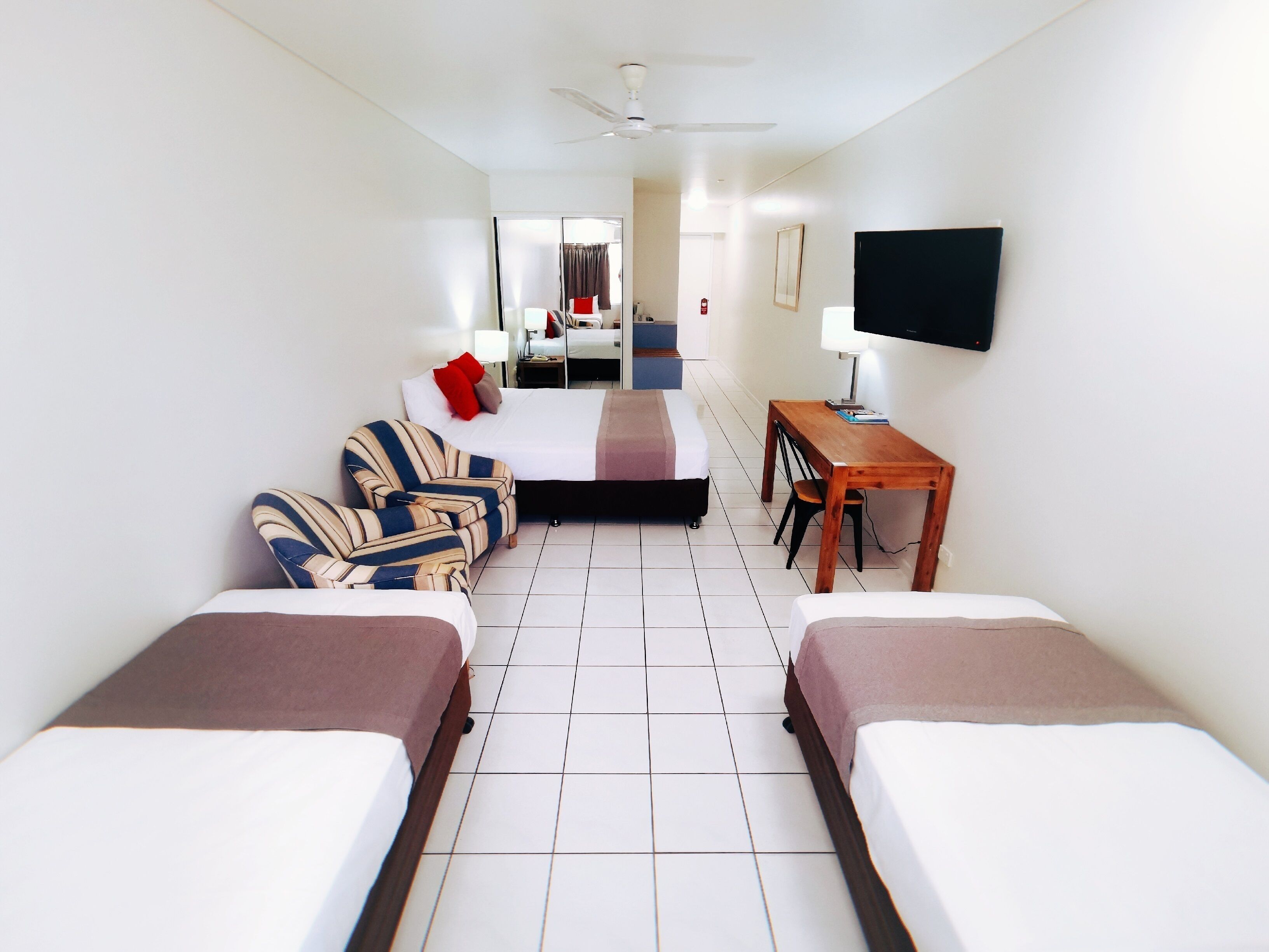 Une chambre d’hôtel avec deux lits, un bureau, une chaise, une télévision et un ventilateur de plafond.