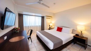 A hotel room with a bed, a desk, a chair, a TV, and a ceiling fan. - Hides Hotel Cairns (Cairns)
