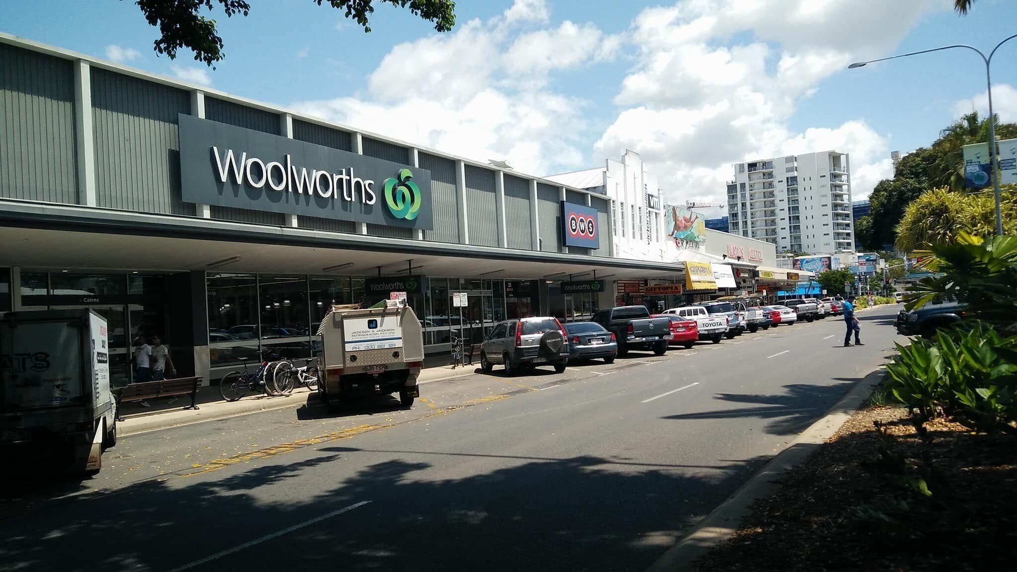 Un magasin Woolworths avec une grande enseigne, un parking et plusieurs voitures garées devant.