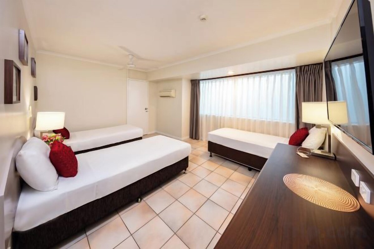 A hotel room with two beds, a desk, a chair, a TV, and a window with curtains.