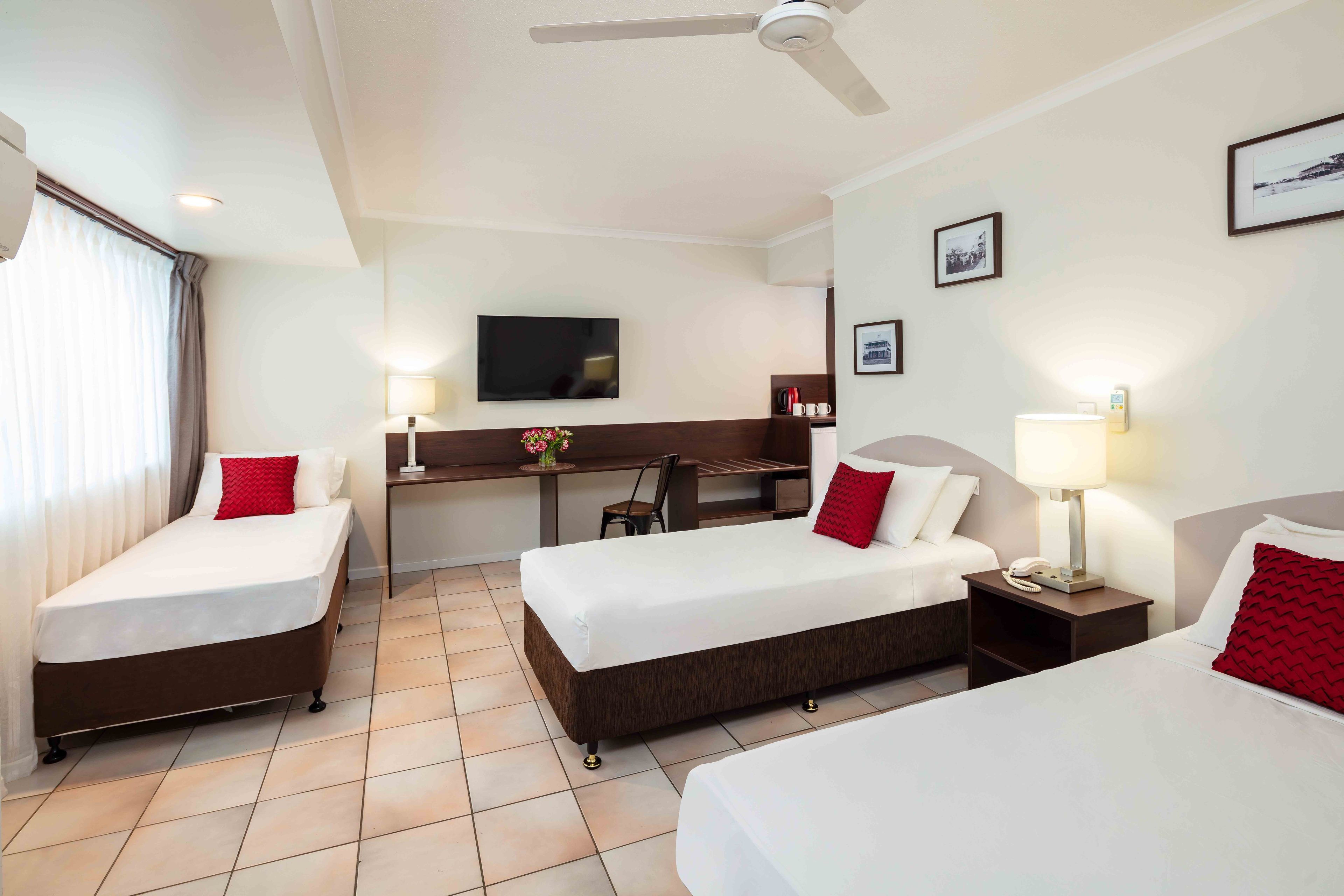 Une chambre d’hôtel avec deux lits simples, un bureau, une chaise, une télévision et un ventilateur de plafond.