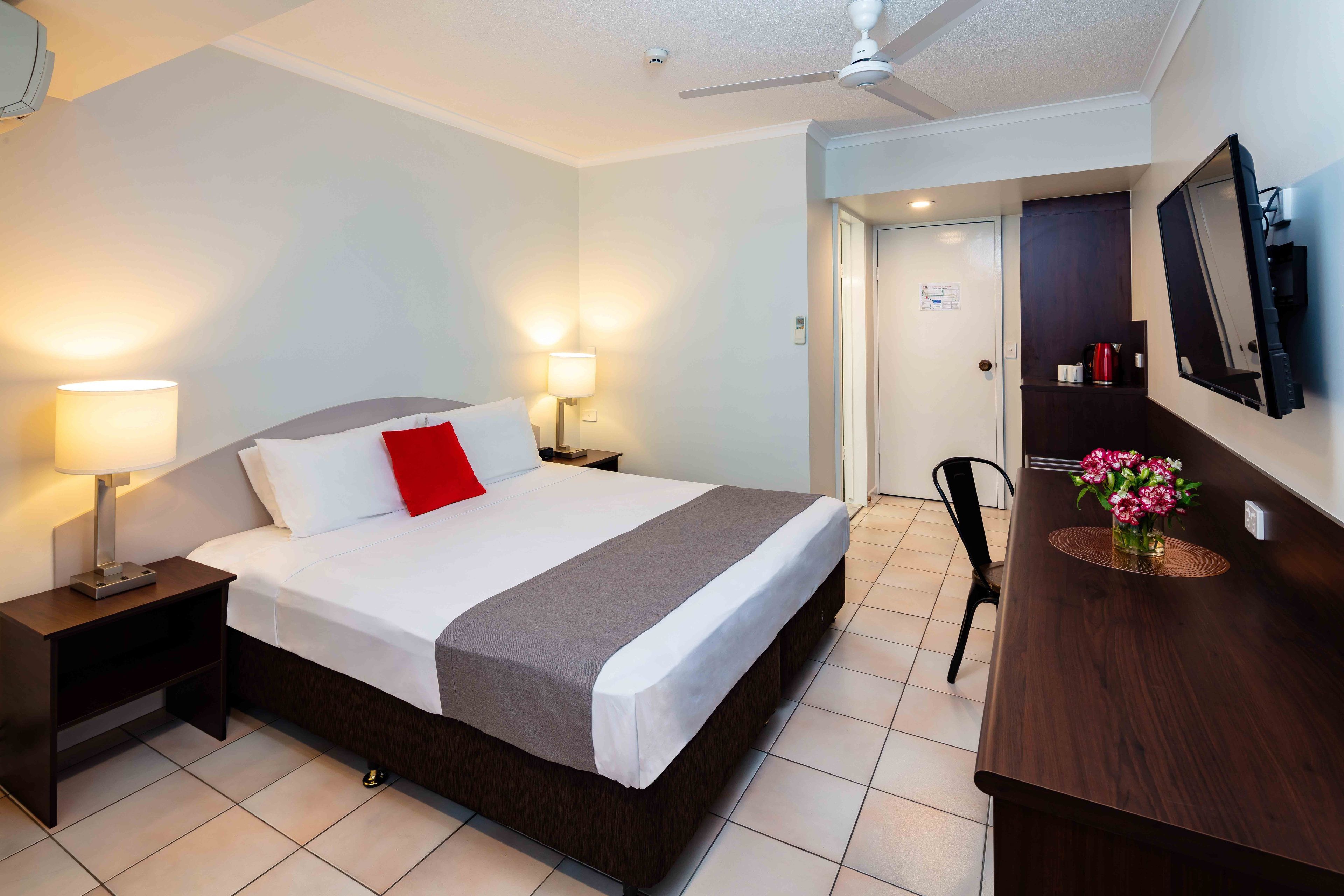 Habitación de hotel con cama, lámparas de noche, escritorio con espejo y ventilador de techo.