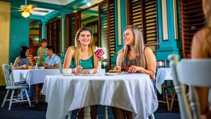A restaurant with tables covered in white tablecloths, wooden chairs, and a ceiling fan. - Hides Hotel Cairns (Cairns)