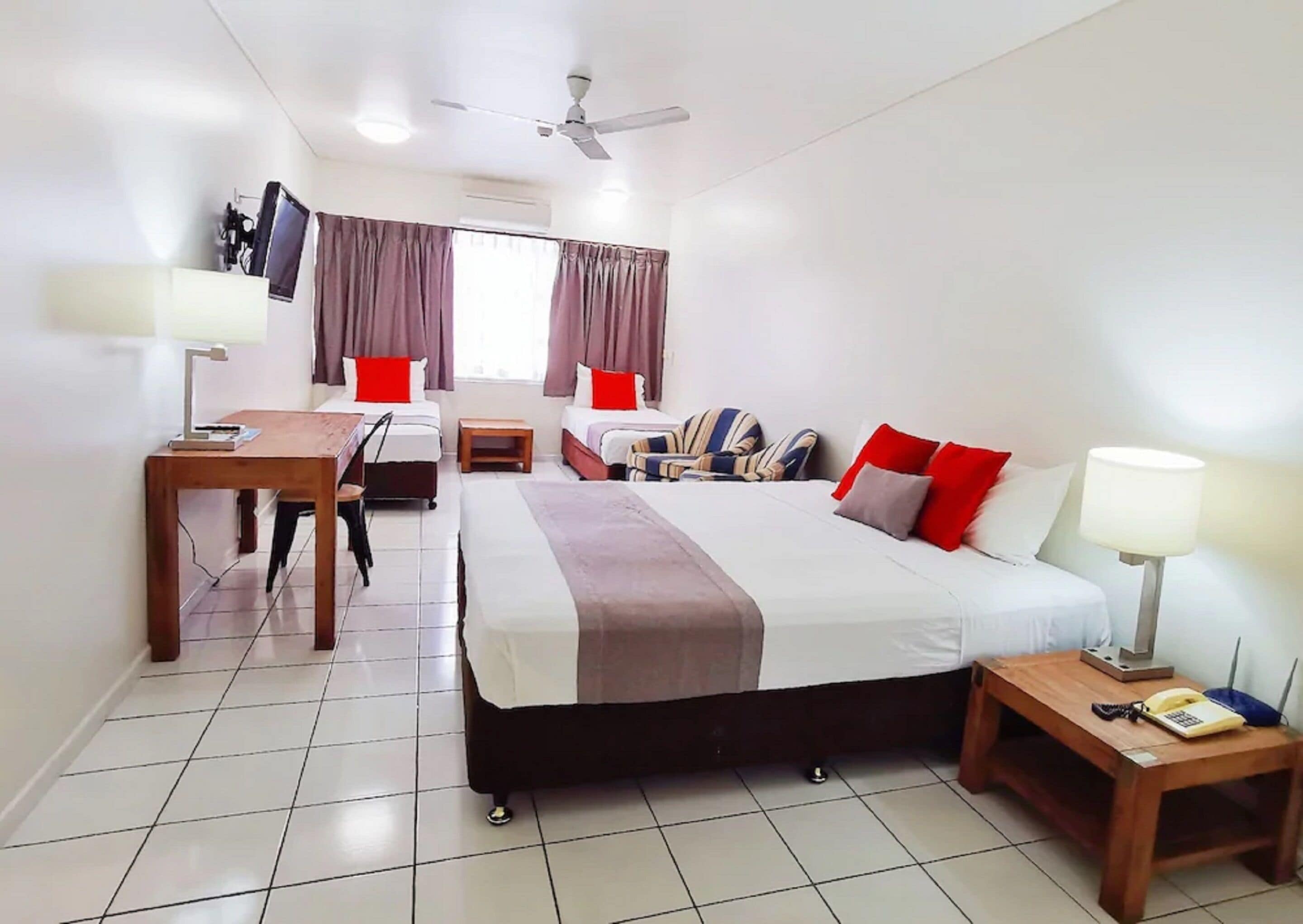 A hotel room with a bed, two bedside tables, a desk with a chair, a TV, and a ceiling fan.