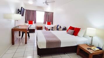 A hotel room with a bed, two bedside tables, a desk with a chair, a TV, and a ceiling fan.