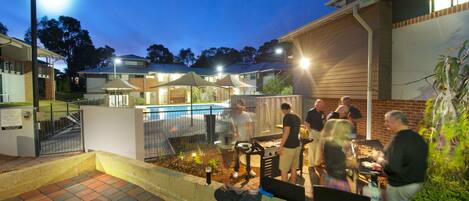 An outdoor patio area with a barbecue setup, a pool, and a brick pathway leading to a gated entrance.
