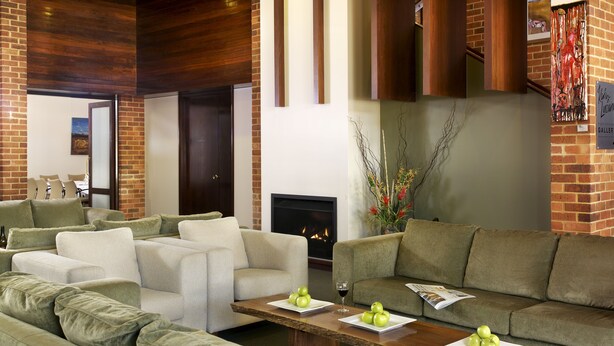 A modern living room with a fireplace, green sofas, and a coffee table with apples and wine glasses. - Margarets in Town Apartments (Margaret River)