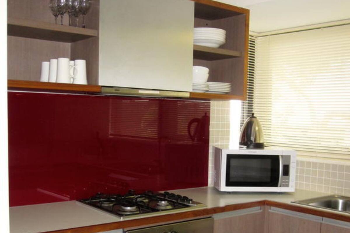 A compact kitchen with a stove, oven, microwave, and a window with blinds.