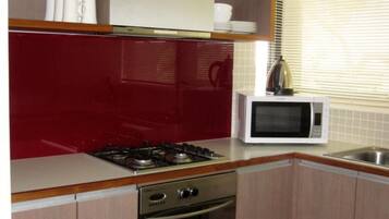Une cuisine compacte équipée d’une cuisinière, d’un four, d’un four à micro-ondes et d’une fenêtre avec des stores.
