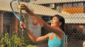 A person playing tennis with a racket and ball, standing in front of a chain-link fence.