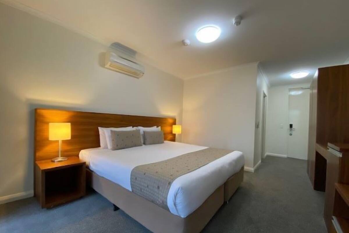 A hotel room with a large bed, two bedside lamps, an air conditioning unit, and a wooden wardrobe.