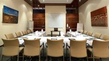 Un salón de conferencias con una larga mesa, sillas y una pantalla de proyector.