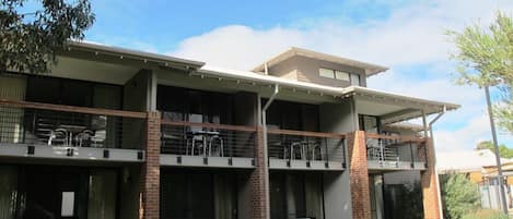 A two-story building with a flat roof, large windows, and a covered outdoor area with tables and chairs.