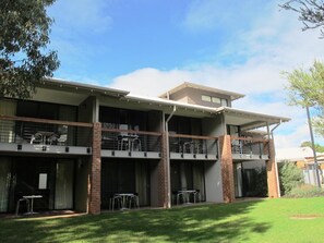 A two-story building with a flat roof, large windows, and a covered outdoor area with tables and chairs.