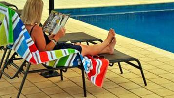 A poolside area with lounge chairs and a person reading a magazine.