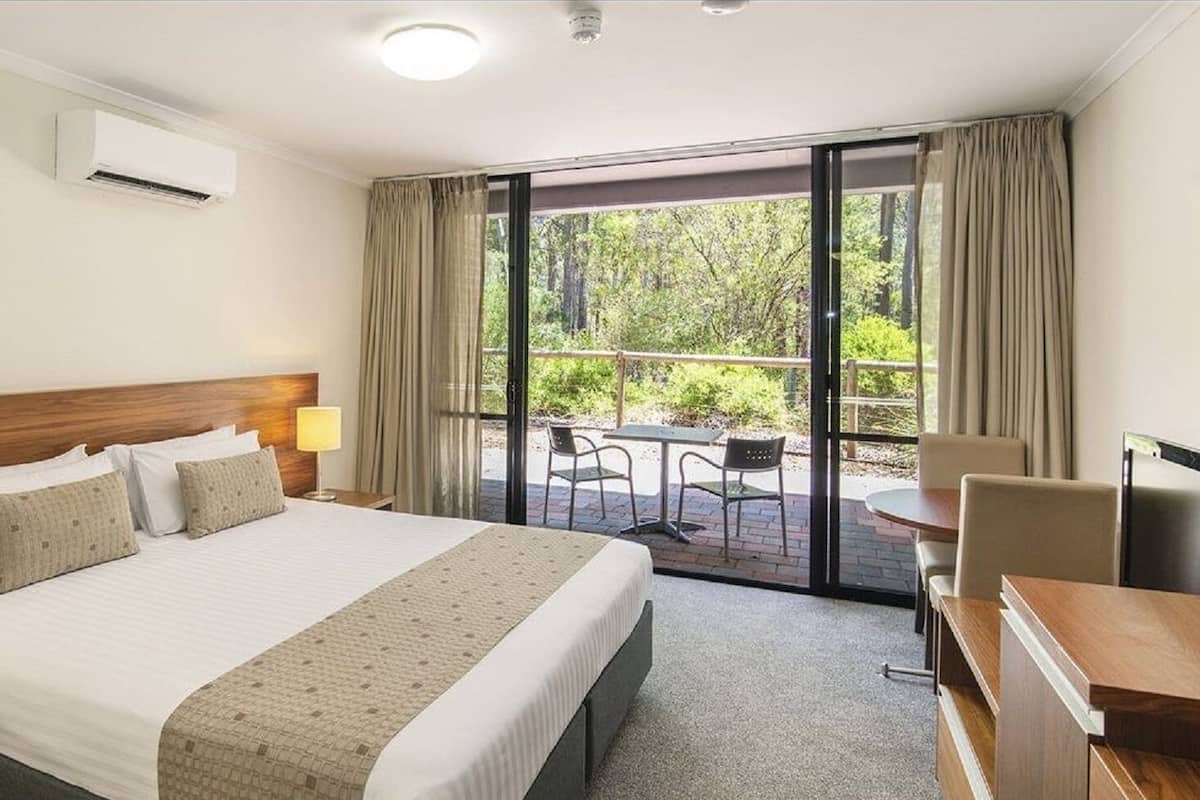 A hotel room with a large bed, a desk, a chair, and a balcony with a table and chairs.