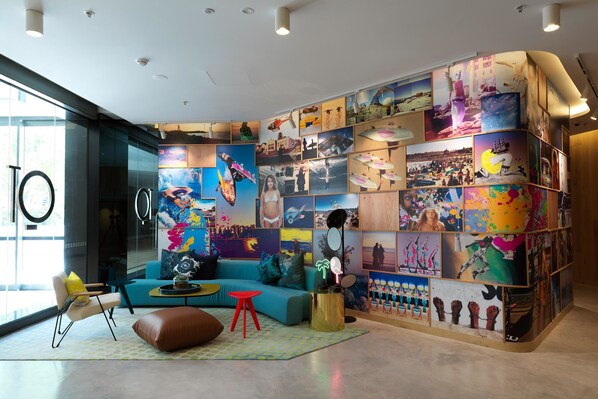 Un moderno vestíbulo de hotel con una gran pared de arte vibrante, un sofá azul, un taburete rojo y una puerta de cristal que da al exterior.