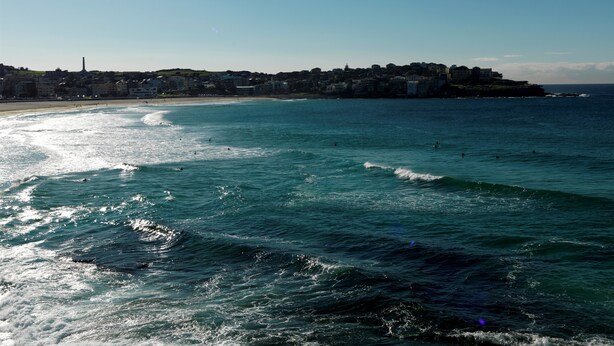 Un pueblo costero con playa, olas del océano y edificios al fondo.