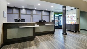 Zona d'entrada d'hotel amb dues taules de recepció, una màquina expenedora i un moble vitrina amb aperitius.
