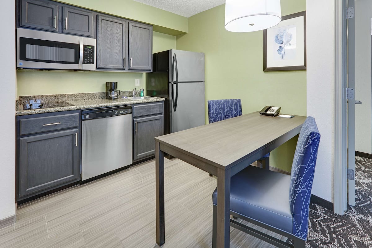 Una cocina compacta con microondas, refrigerador y lavavajillas. Hay una mesa de comedor con una silla y una lámpara colgante.