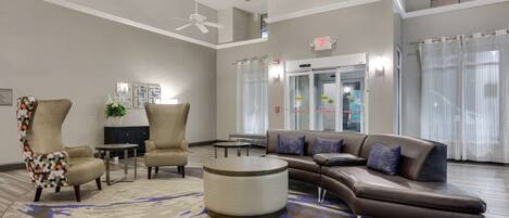 Un vestíbulo amplio con un sofá de cuero marrón grande, dos sillones, una mesa redonda para café y una alfombra estampada.
