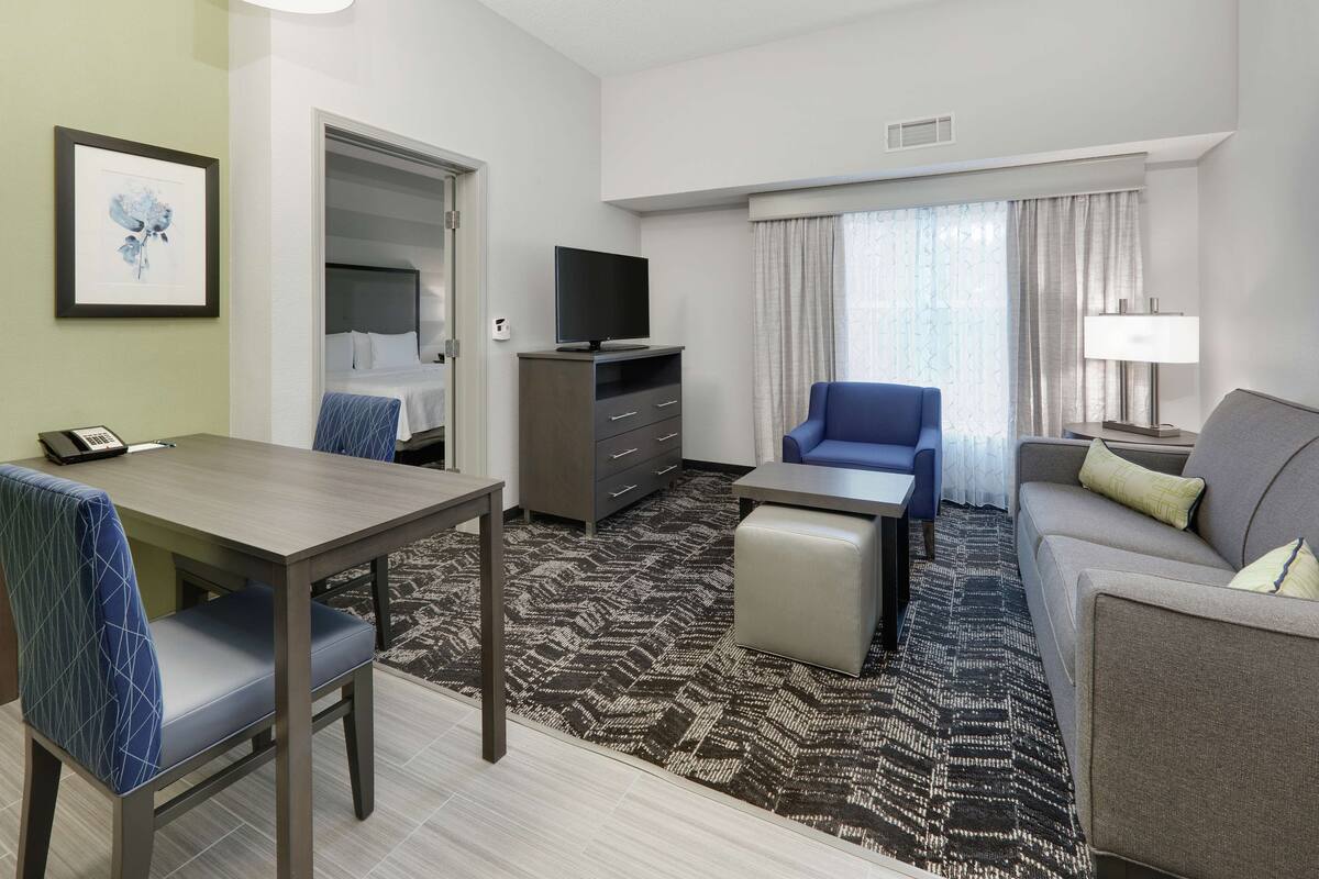Habitación de hotel con una mesa de comedor, dos sillas, un sofá, un televisor, un escritorio y una lámpara.