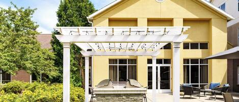 A building with a yellow facade, a covered patio with a grill, and outdoor seating.